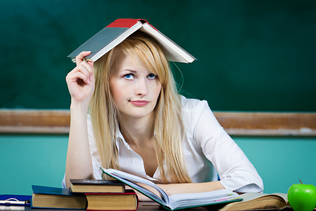 Annoyed funny looking student with book on head, sitting at desk