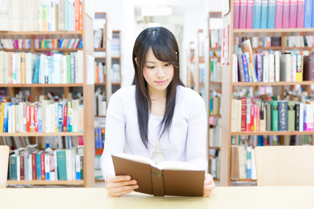 young asian woman reading a book in the library
